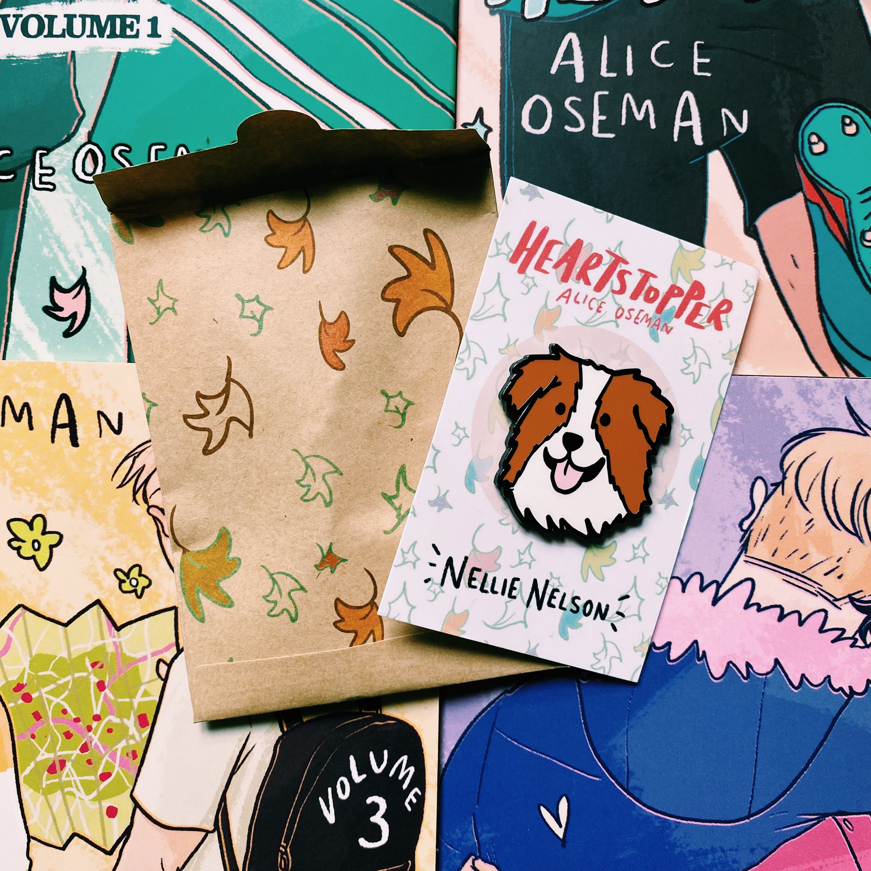 Nellie Nelson enamel pin inspired by Alice Oseman's Heartstopper series. The pin is being held in front of the Hearstopper graphic novels and exclusive LitPins packing paper.