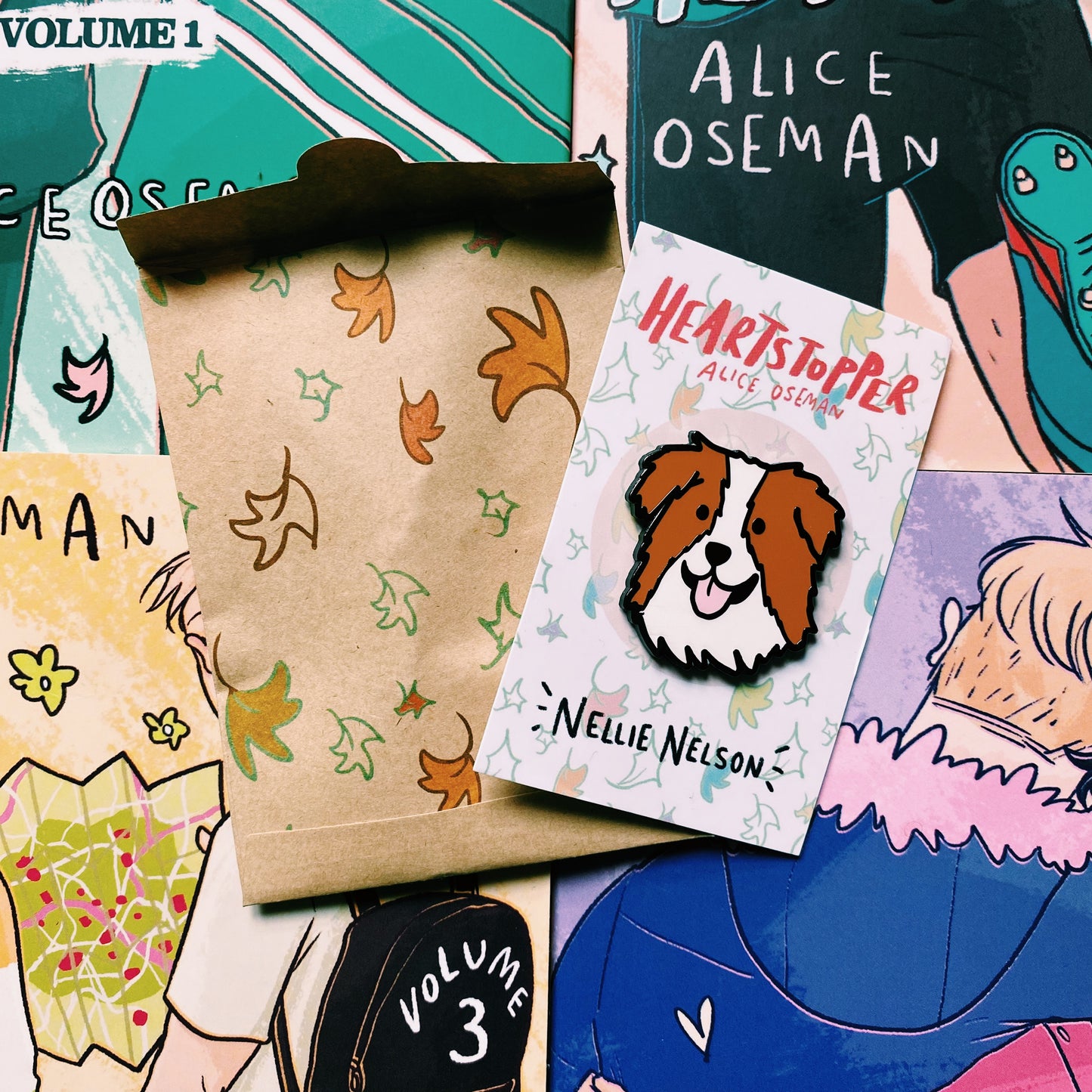 Nellie Nelson enamel pin inspired by Alice Oseman's Heartstopper series. The pin is being held in front of the Hearstopper graphic novels and exclusive LitPins packing paper. 