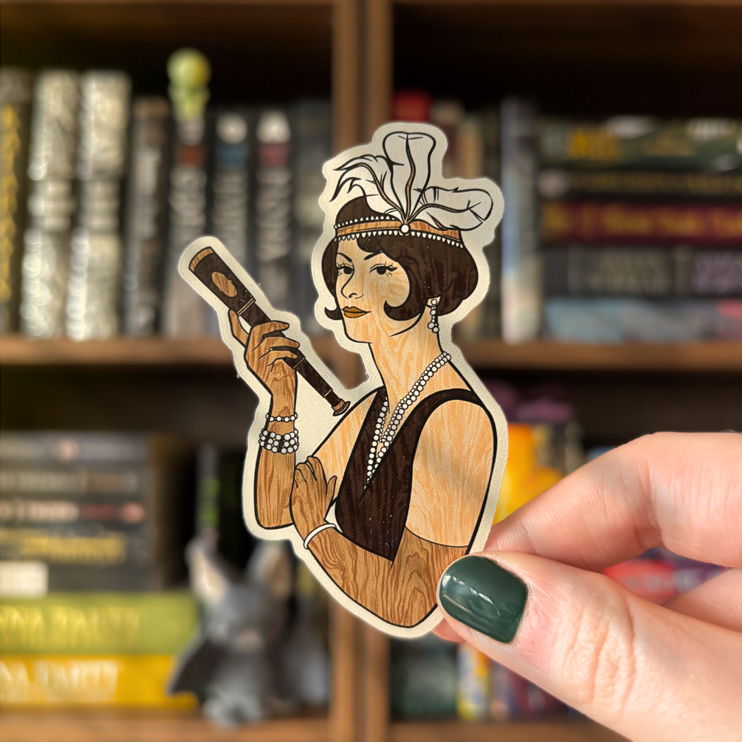 A sticker featuring the Darcy figurehead from the Vampirates series, held in front of a background of bookshelves