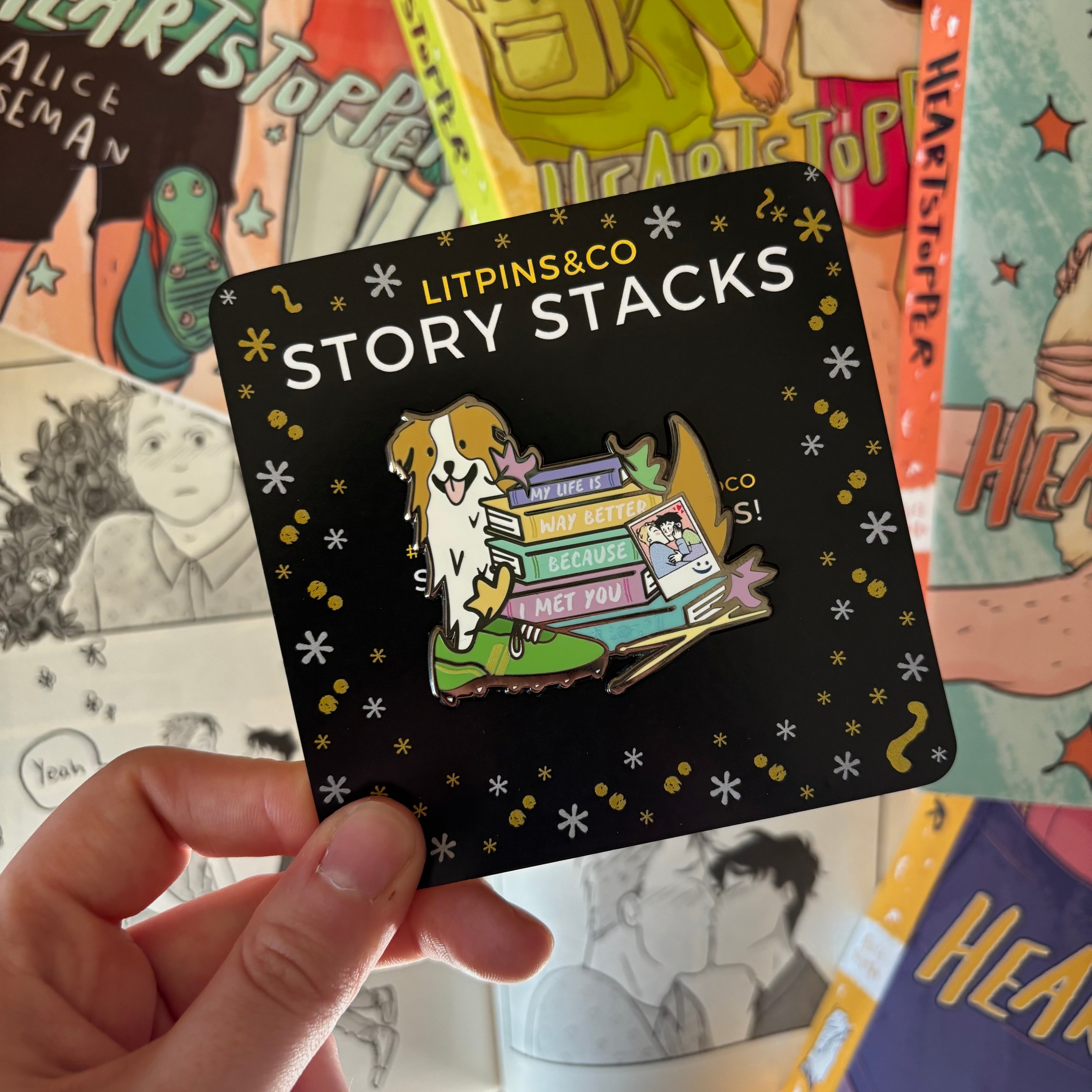Story stack enamel pin inspired by Heartstopper by Alice Oseman, pictured against the Heartstopper graphic novels.