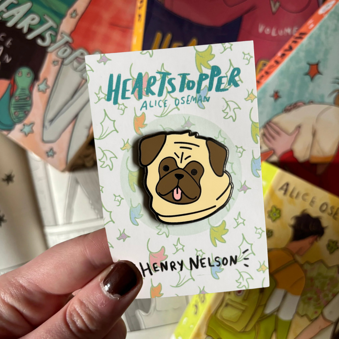 Pin with a pug design on a 'Heartstopper' card held in front of the Heartstopper graphic novels.