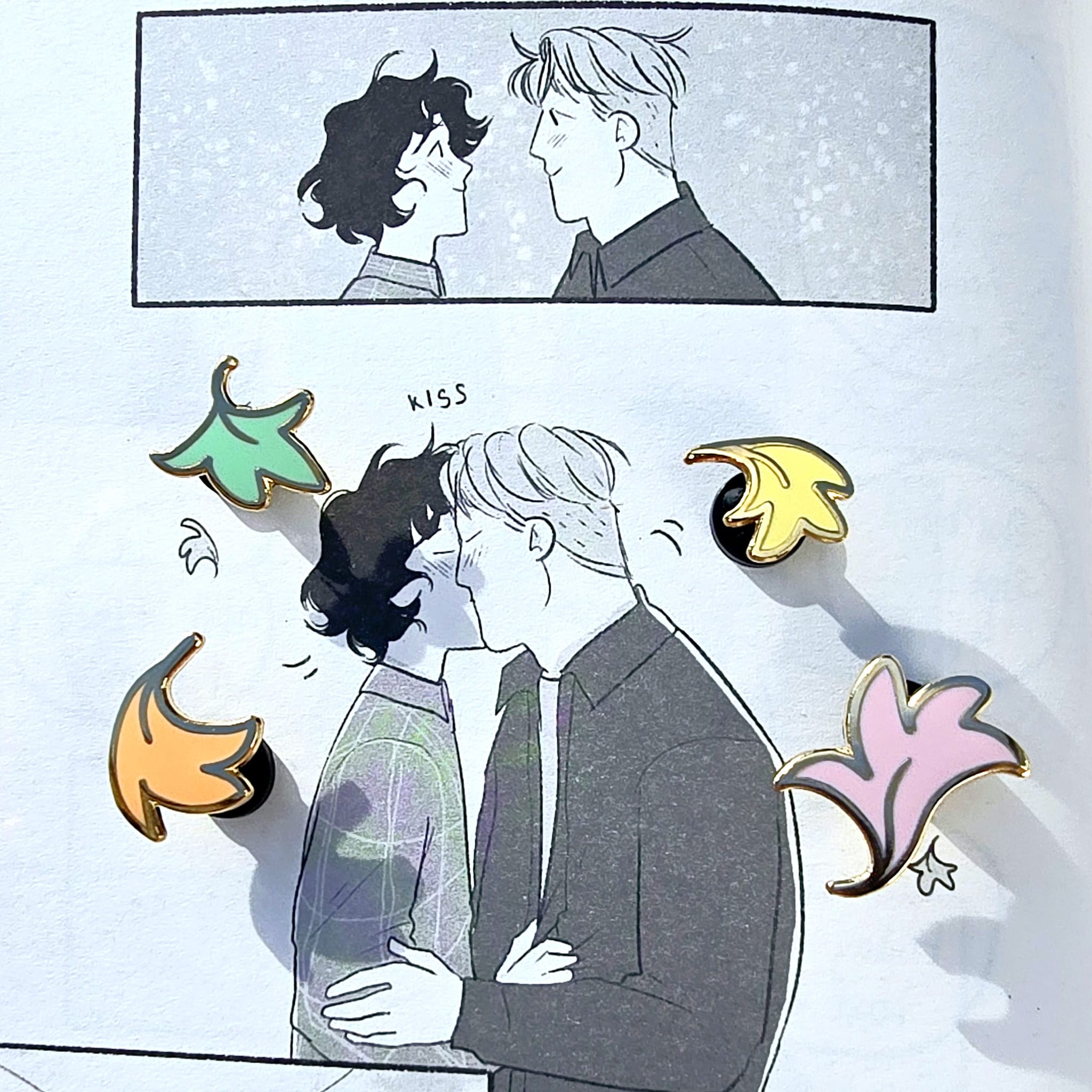 The Officially Licenced Mini Leaf Enamel Pins resting against a page from Hearstopper by Alice Oseman covering were the illustration of the leaves are.