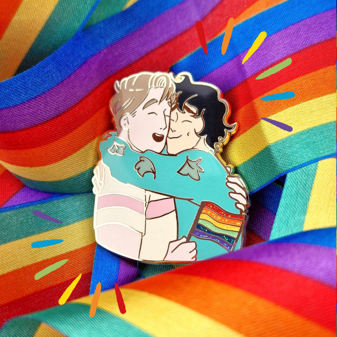 Officially licensed Heartstopper pride pin. Features Nick and Charlie in an embrace with Nick holding a Pride Flag., designed by Alice Oseman.