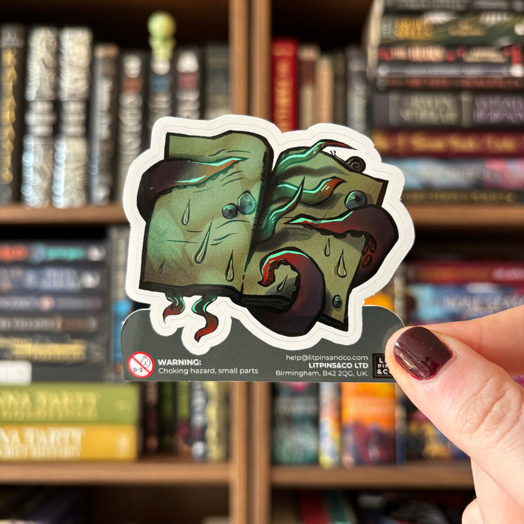 A die-cut sticker featuring an open book which is being torn apart by blue and red toned tentacles. The book also has water drops and barnacles on it. The sticker is pictured held against a blurred background.