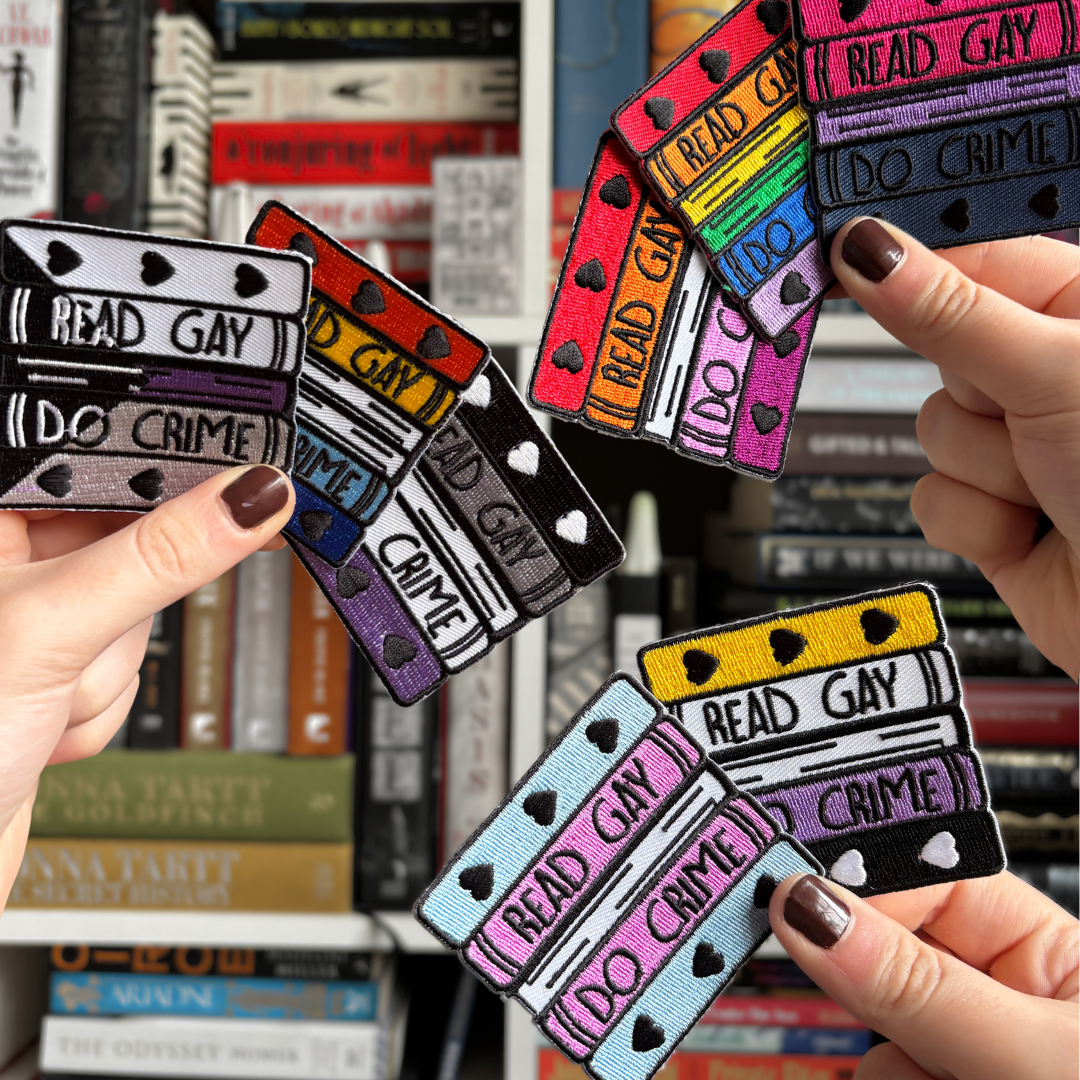 LitPIns&Co Read Gay Do Crime Patches against open books with the newest enamel pins resting on top of them.