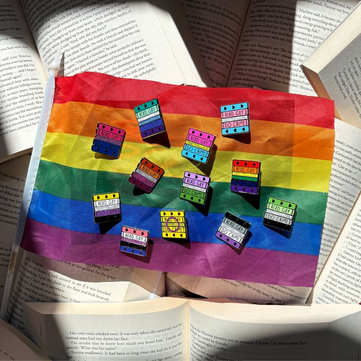 The Read Gay Do Crime Pride Pin Collection resting against the pride flag on top of a background of opened books.