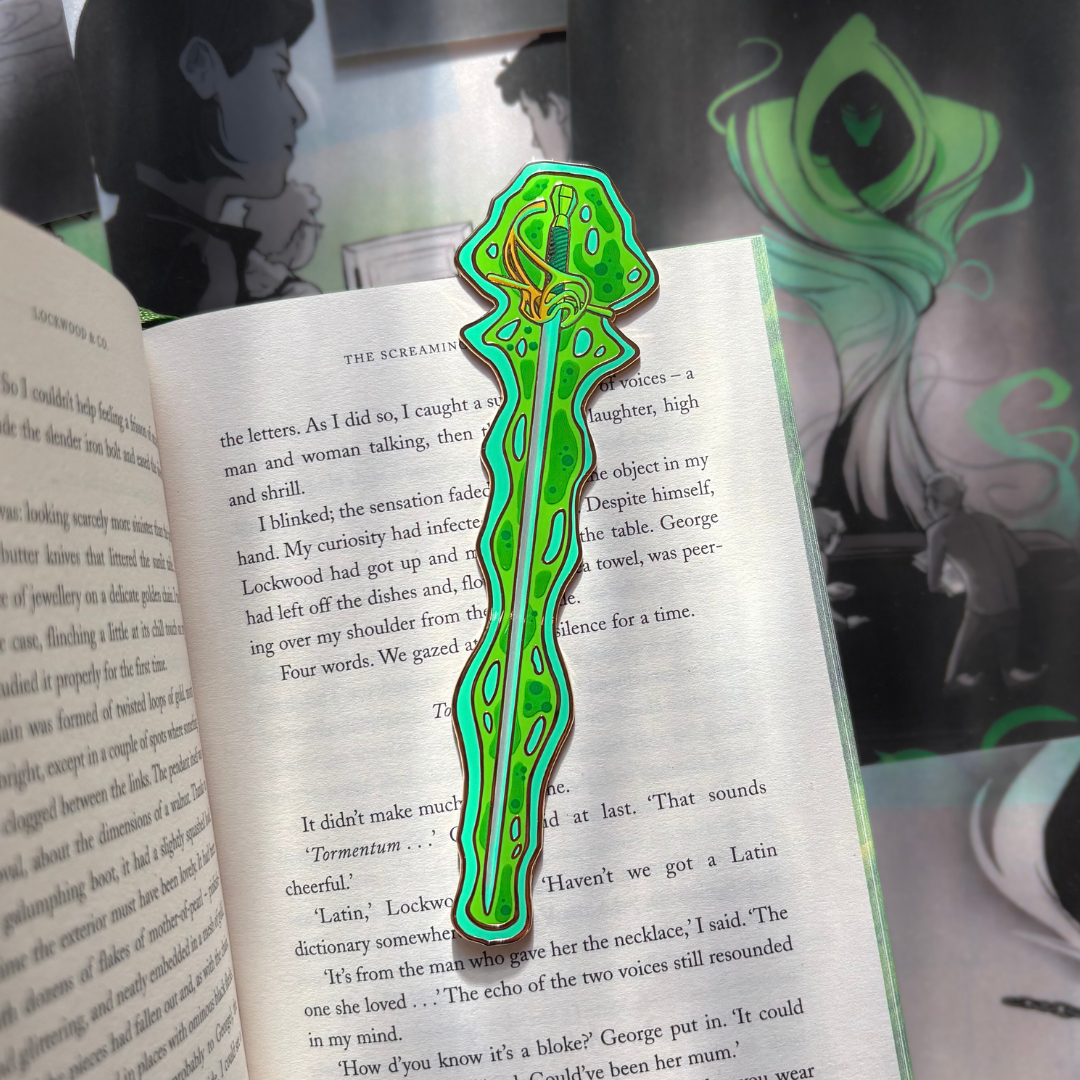 A green enamel bookmark shaped like a sword surrounded by ectoplasm, photographed against the LitPins&Co special edition of Lockwood&Co