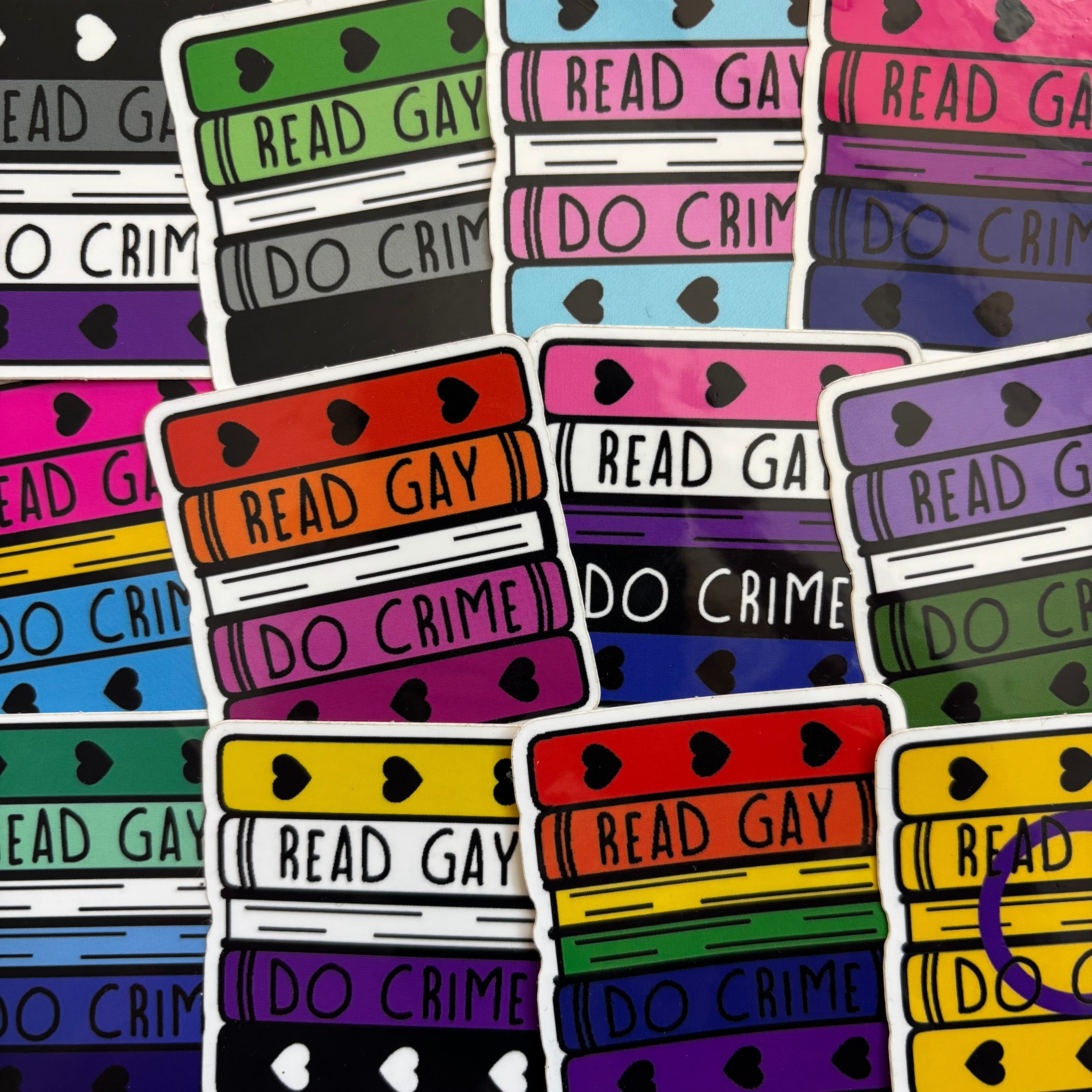 Book shaped stickers featuring pride flag designs and the text "Read Gay Do Crime"