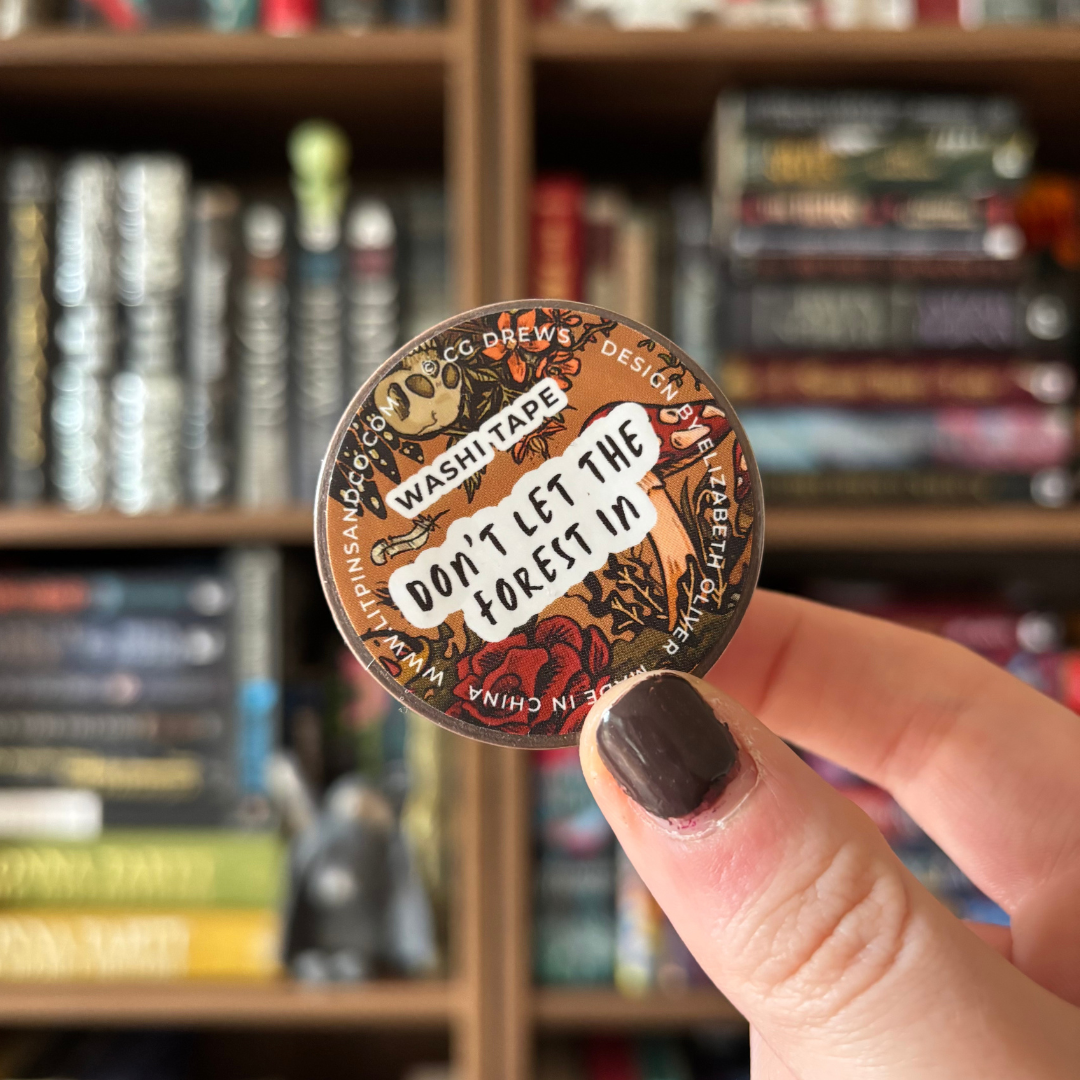 A roll of botanical horror washi tape held against a blurred bookshelf