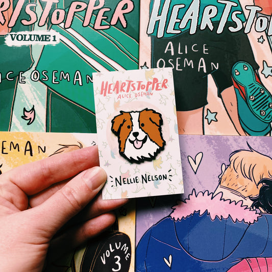 Nellie Nelson enamel pin inspired by Alice Oseman's Heartstopper series. The pin is being held in front of the Hearstopper graphic novels. 