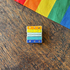 Pin with 'Read Gay, Do Crime' text on a wooden surface with a rainbow fabric background