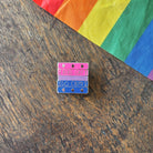 Pin with 'Read Gay, Do Crime' text on a wooden surface with a rainbow fabric background