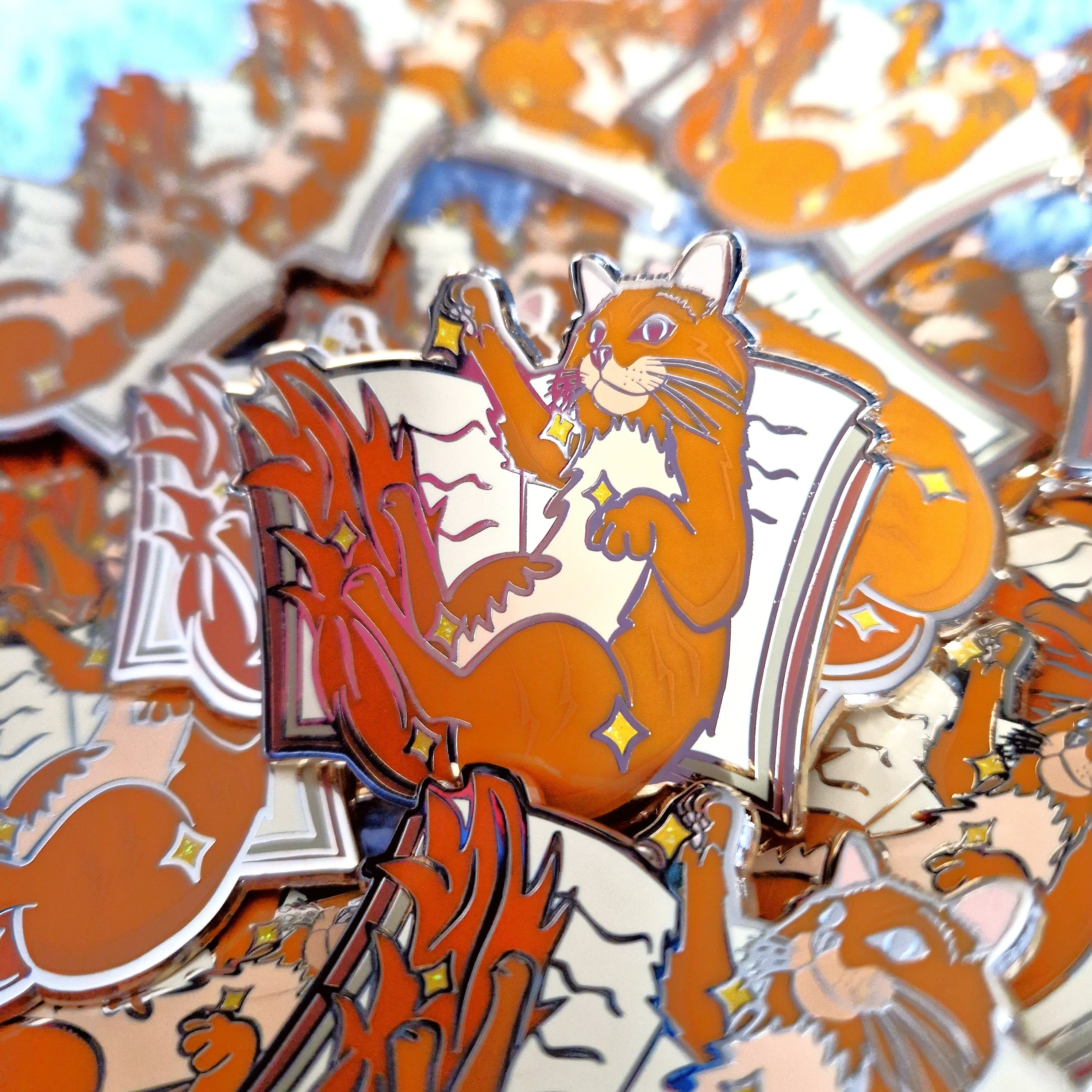 Enamel pins inspired by Book the cat from V. E. Schwab's Addie LaRue, featuring a cat pictured against an open book.
