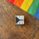 Pin with 'Read Gay, Do Crime' text on a wooden surface with a rainbow fabric background