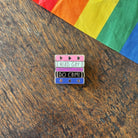 Pin with 'Read Gay, Do Crime' text on a wooden surface with a rainbow fabric background