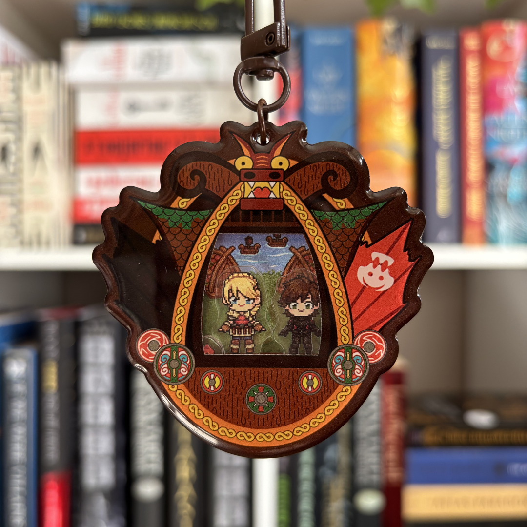 Decorative shaker keychain with characters from the How To Train Your Dragon books in a decorative frame against a bookshelf background
