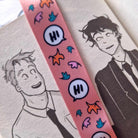 Pink lanyard inspired by Heartstopper by Alice Oseman. Decorated with cartoon speech bubbles reading "Hi" and leaves. Pictured against a background of the Heartstopper graphic novels.