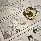 The Henry Nelson enamel pin ressting on the open pages of the Heartstopper graphic novel on the page which Nick is lying in bed with Nellie and Henry on his phone. 