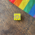 Pin with 'Read Gay, Do Crime' text on a wooden surface with a rainbow fabric background