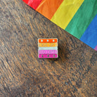 Pin with 'Read Gay, Do Crime' text on a wooden surface with a rainbow fabric background