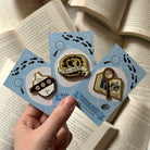 Officially licensed LitPins&Co Murder Most Unladylike collection, held against a background of blurred books