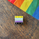 Pin with 'Read Gay, Do Crime' text on a wooden surface with a rainbow fabric background