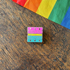 Pin with 'Read Gay, Do Crime' text on a wooden surface with a rainbow fabric background