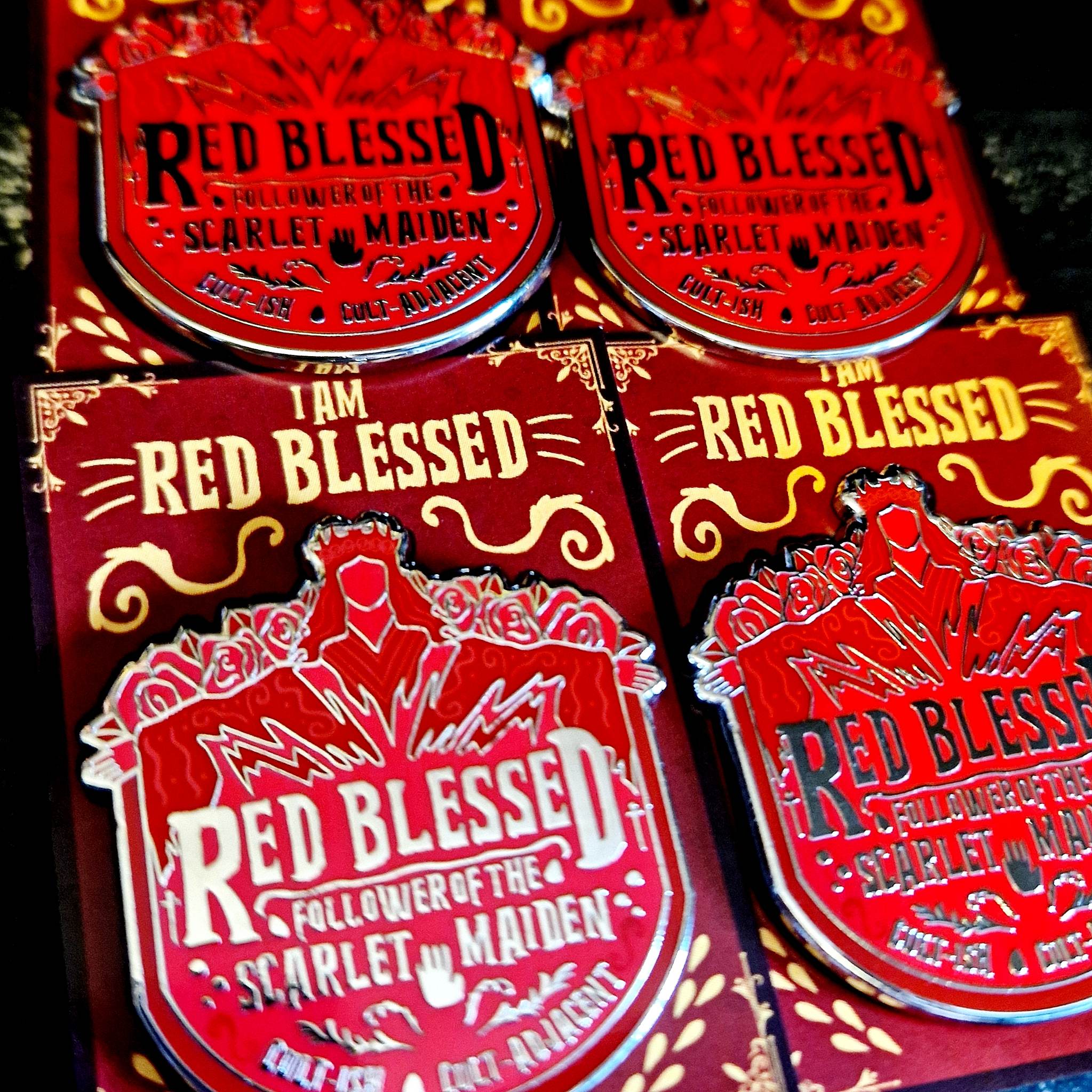 Red enamel pins reading "red blessed follower of the scarlet maiden, cult-ish, cult-adjacent," inspired by Painted Devils by Margaret Owen