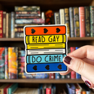 A large sticker designed to look like a stack of books in the colours of the aromantic and asexual pride flag, with text reading "Read Gay Do Crime"