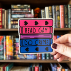 A large sticker designed to look like a stack of books in the colours of the bisexual pride flag, with text reading "Read Gay Do Crime"