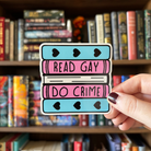 A large sticker designed to look like a stack of books in the colours of the transgender pride flag, with text reading "Read Gay Do Crime"
