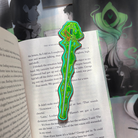 A green enamel bookmark shaped like a sword surrounded by ectoplasm, photographed against the LitPins&Co special edition of Lockwood&Co