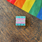 Pin with 'Read Gay, Do Crime' text on a wooden surface with a rainbow fabric background