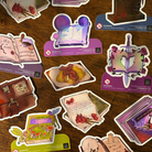 A selection of book shaped stickers themed around various genres, pictured on a wooden background.