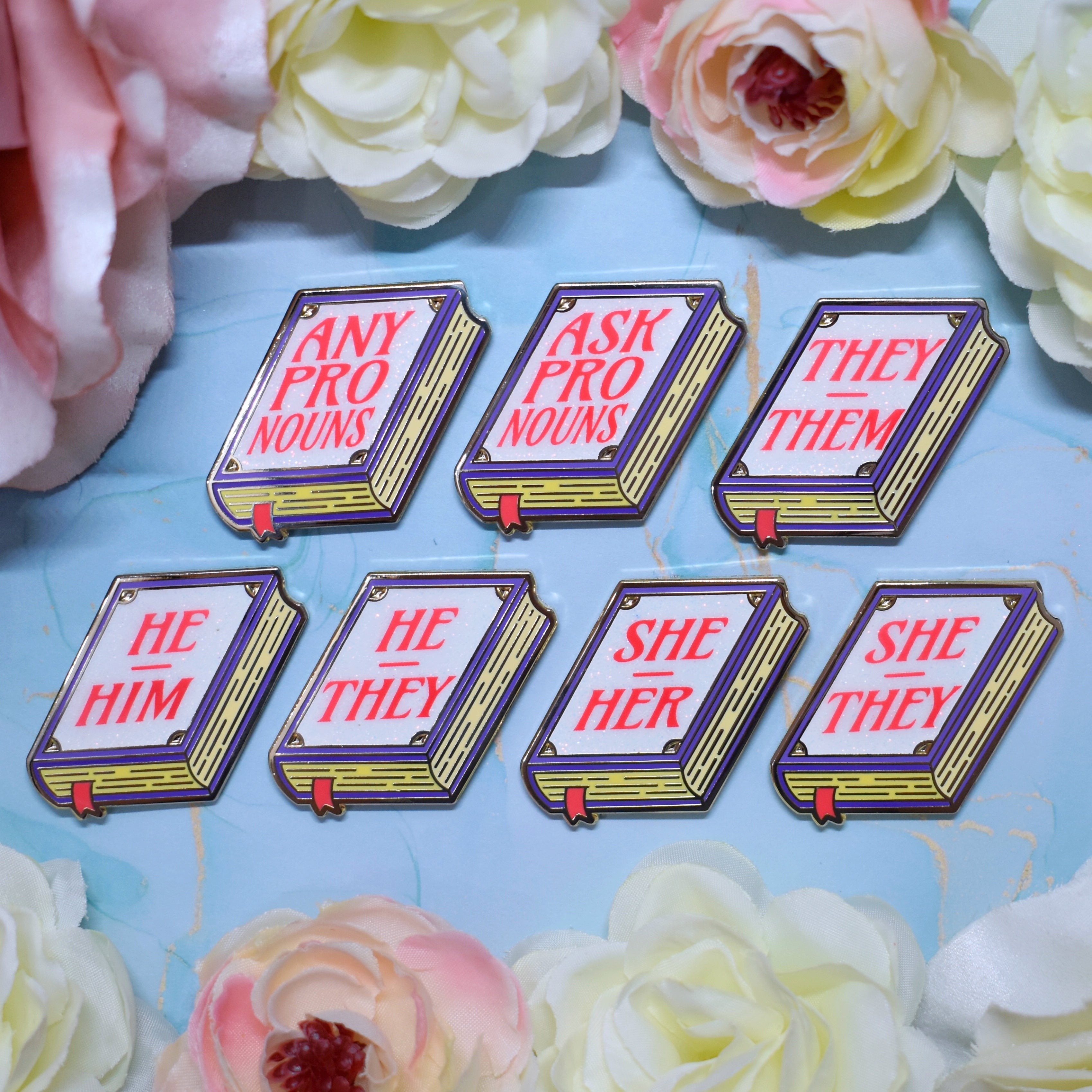 Set of book shaped pronoun pins on a decorative background with flowers