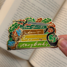 Enamel pin inspired by The Cruel Prince by Holly Black, reading "Nice things don't happen in storybooks." Held against a background of open books.
