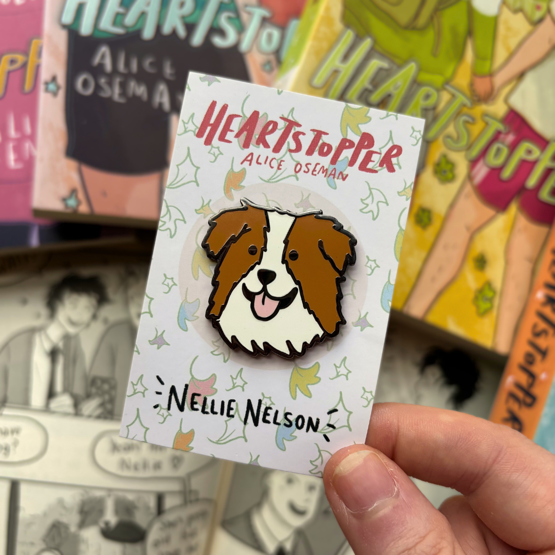 Nellie Nelson enamel pin inspired by Alice Oseman's Heartstopper series. The pin is being held in front of the Hearstopper graphic novels.