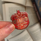 A red enamel pin reading "red blessed follower of the scarlet maiden, cult-ish, cult-adjacent," inspired by Painted Devils by Margaret Owen