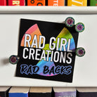 A sign reading "Rad Girl Creations Rad Backs", magnetically held up by four Rad Backs
