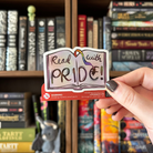 Book-shaped sticker with the text "Read with pride" decorated in colours of various pride flags