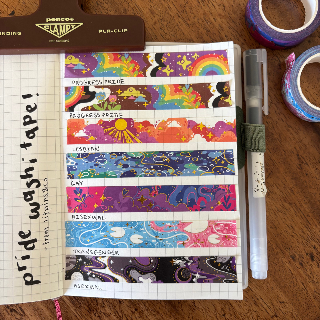 A set of colourful washi tapes inspired by various pride flags, displayed on a grid notepad and surrounded by various pieces of stationary
