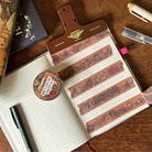 An open journal page decorated with brown washi tape. The washi tape features a dark botanical design of flowers, bones, mushrooms, leaves, and more.