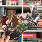 Five wooden bookmarks inspired by the Empire of the Vampire series, held in front of a bookshelf