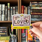 Book-shaped sticker with the text "you are LOVED" decorated in colours of various pride flags