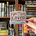 Book-shaped stickers with the text "you are LOVED" decorated in colours of various pride flags