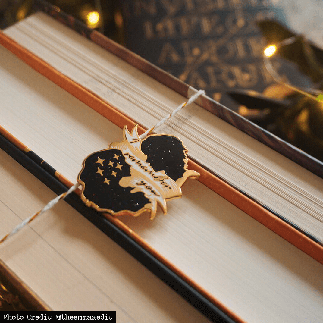 I Remember You, The Invisible Life of Addie LaRue by V.E Schwab enamel pin resting against the spines of books.